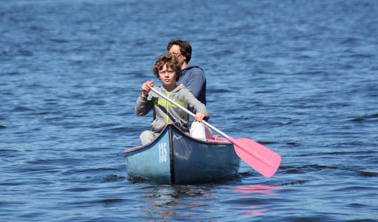 On a canoe, paddlers grip a single-bladed paddle, alternating strokes on ei...